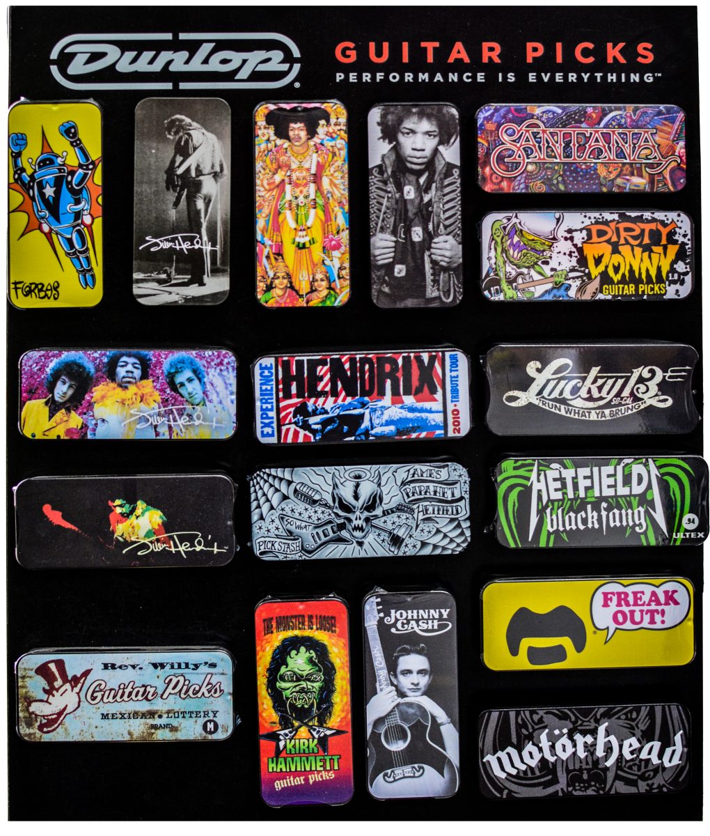 A black retail display board showcasing sixteen rectangular Jim Dunlop guitar pick tins. The metal tins feature colorful graphic artwork and logos for various artists and brands, including Jimi Hendrix, Santana, Dirty Donny, James Hetfield Black Fang, Johnny Cash, Kirk Hammett, and Motörhead.
