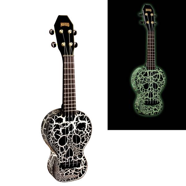 A Mahalo soprano ukulele featuring a skull-shaped black and white crackle finish on the body, a black headstock with a gold logo, and gold geared tuners with black buttons. An inset image on the right displays the identical ukulele glowing bright green against a solid black background.