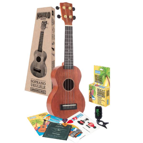A Mahalo MJ1TBRK soprano ukulele in a natural matte finish, pictured alongside its packaging box and the Mahalo Essentials Accessory Pack which includes a clip-on tuner, three picks, Aquila strings, and a sticker sheet.